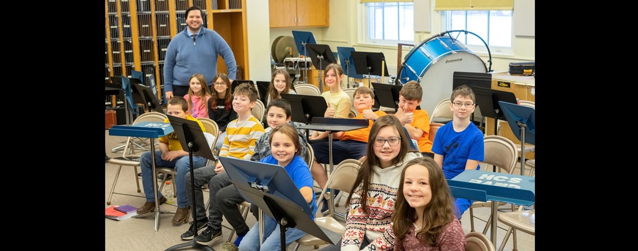 Students in band class pose near instruments with teacher 