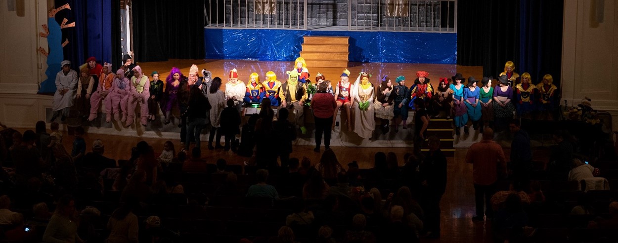 Students sit on stage following a performance of Shrek